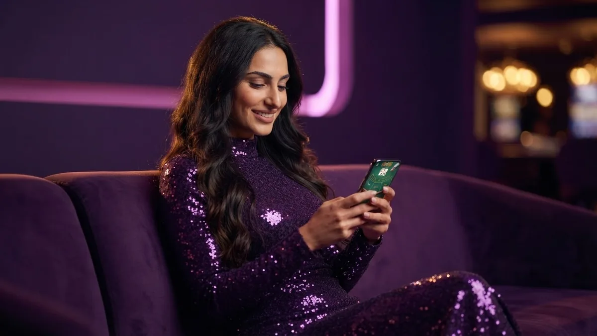 A croupier relaxing on a lounge sofa with a phone, the screen shows a drawn baccarat game with virtual chips